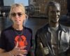 Woman with sunglasses standing beside a shiny silver statue that is giving a thumbs up, by a waterfront in a city.