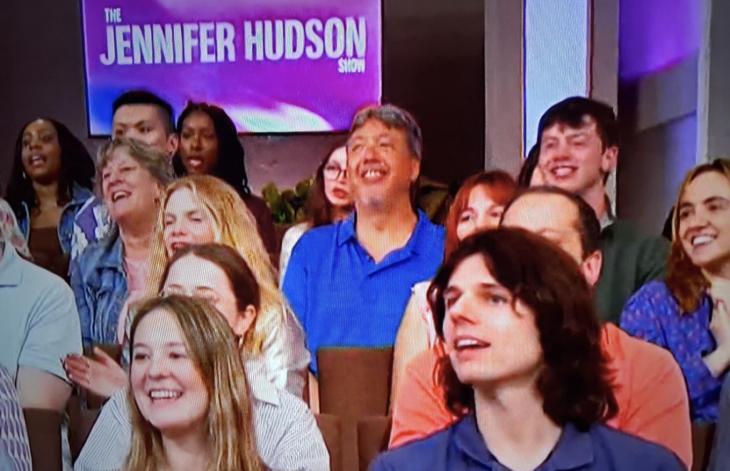 Audience members smiling and looking toward the stage on The Jennifer Hudson Show set, with the show's purple logo in the background.