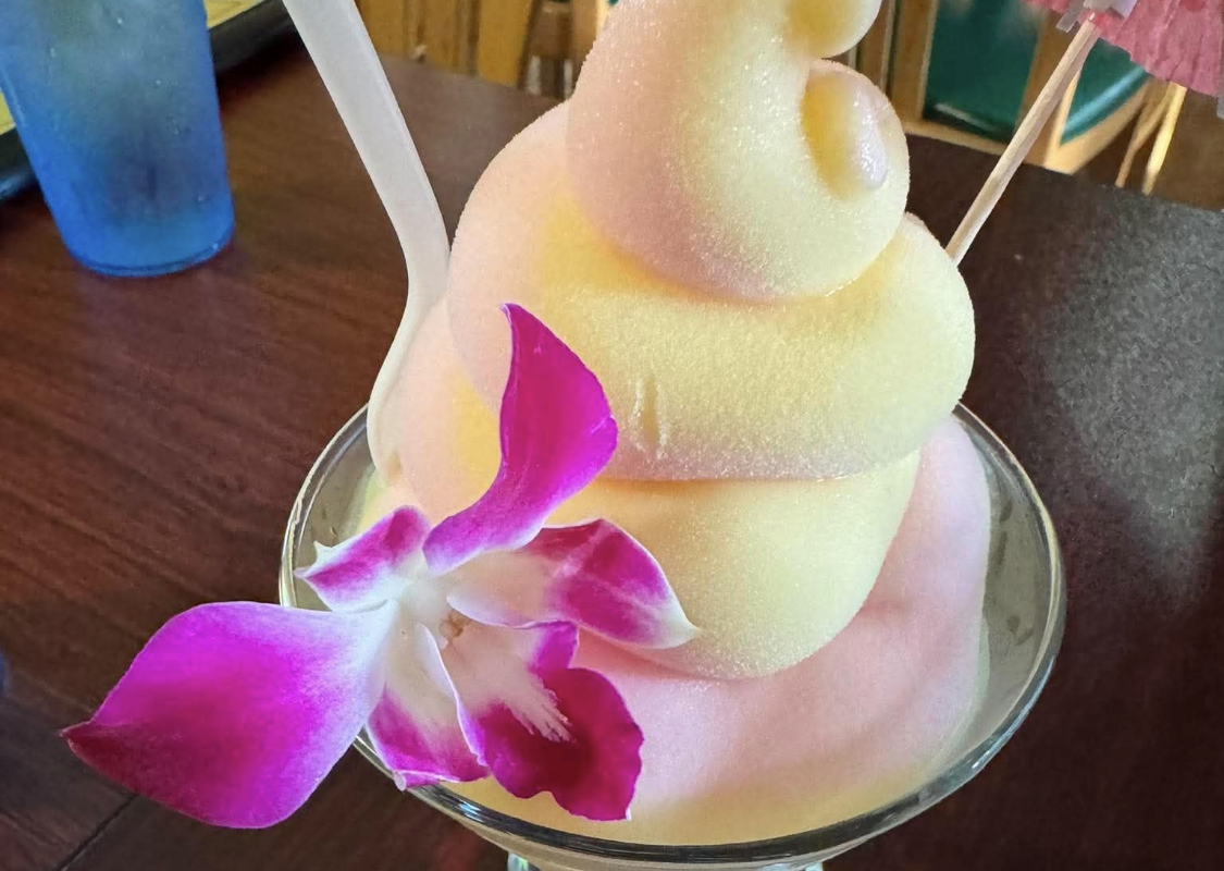 Tropical cocktail with yellow and pink layered soft-serve ice cream in a stemmed glass, garnished with a pink orchid orchid and a small umbrella.