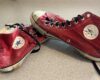 Red Converse All Star high-top sneakers with black laces, worn and scuffed, resting on a light floor.