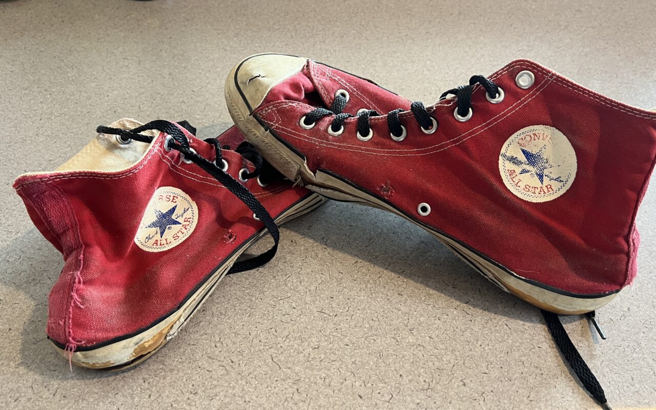 Red Converse All Star high-top sneakers with black laces, worn and scuffed, resting on a light floor.
