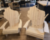 Two unfinished wooden Adirondack chairs shaped like the United States map, displayed in a workshop or store setting.