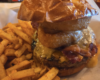 Juicy burger with melted cheese and bacon, topped by a fried onion ring, served with seasoned fries on the side