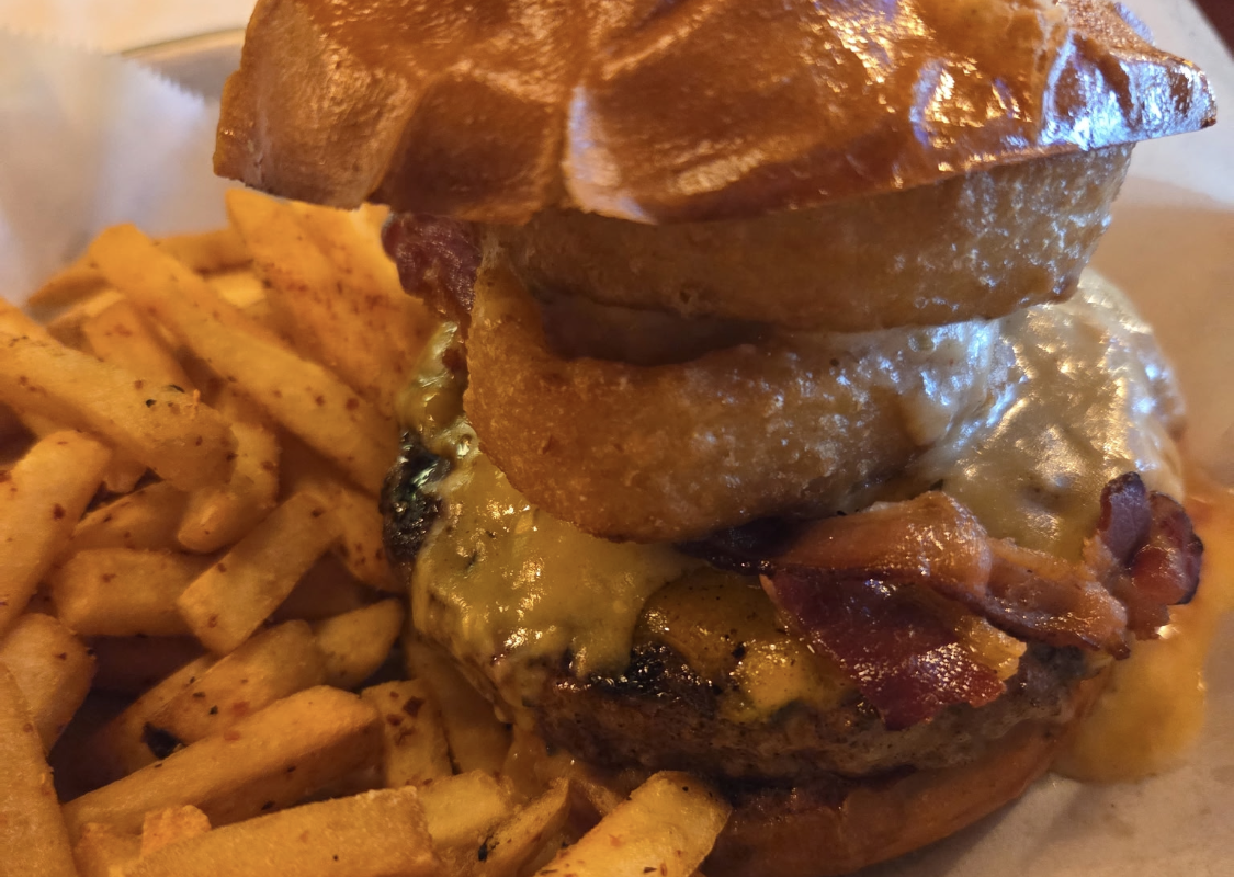 Juicy burger with melted cheese and bacon, topped by a fried onion ring, served with seasoned fries on the side