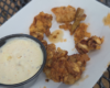 Crispy fried chicken bites arranged on white parchment with a cup of creamy ranch-style dipping sauce nearby.
