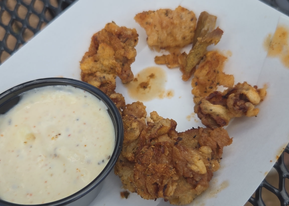 Crispy fried chicken bites arranged on white parchment with a cup of creamy ranch-style dipping sauce nearby.
