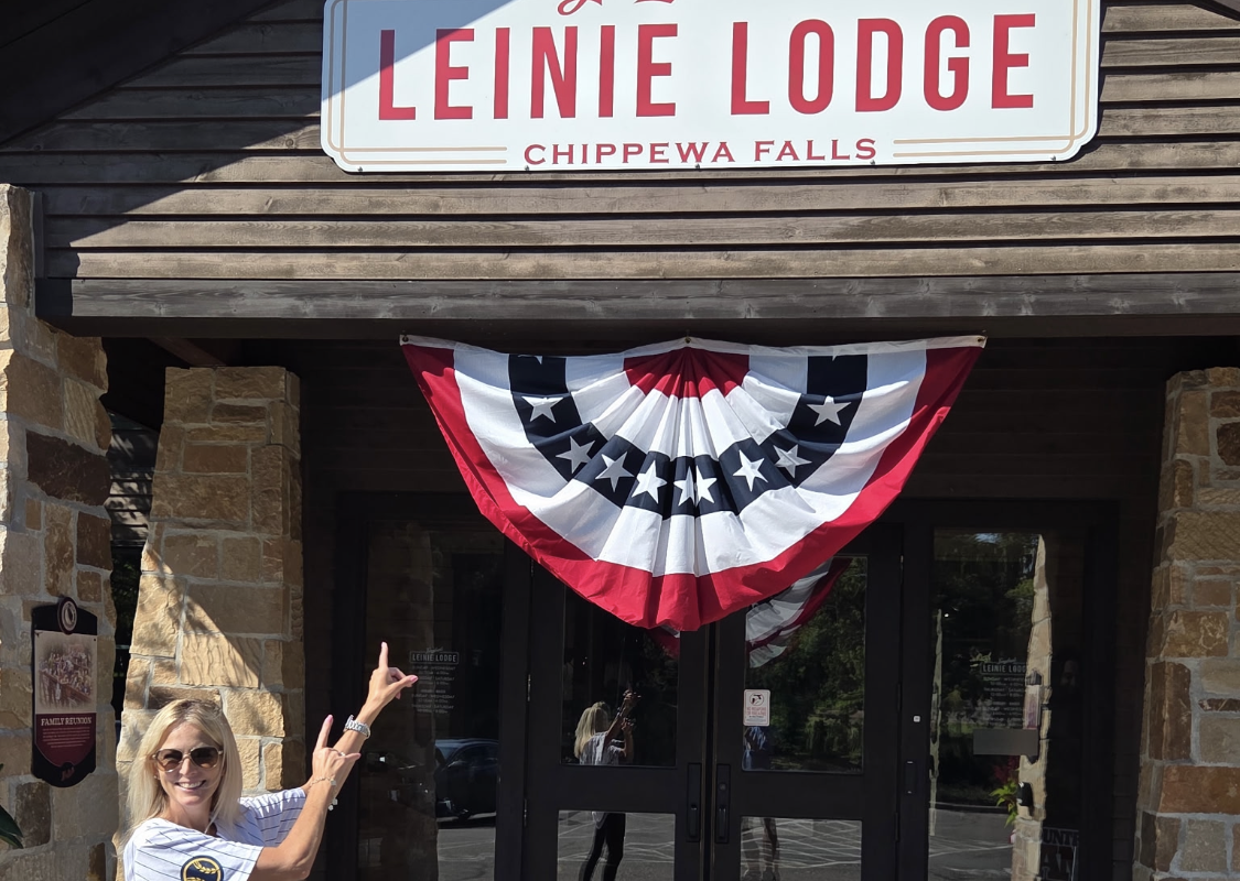 Woman in sunglasses points at the Leinie Lodge sign above a doorway with patriotic bunting.