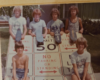 Six teenagers posing with skateboards on top of large 'No Parking or Standing' signs outdoors.