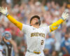 Baseball player in Brewers uniform raises arms in celebration as fans cheer in the background.